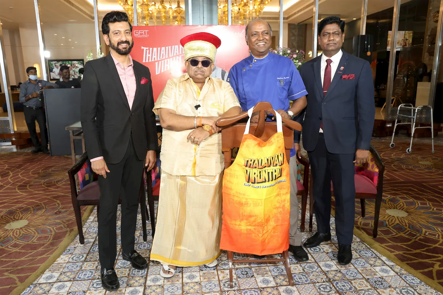 Padma Shri Dr. Chef Damu in traditional attire with Chef Sheetharam Prasad and team at the launch of Thalaivan Virunthu 3.0, Grand Chennai by GRT Hotels, with a branded apron on display