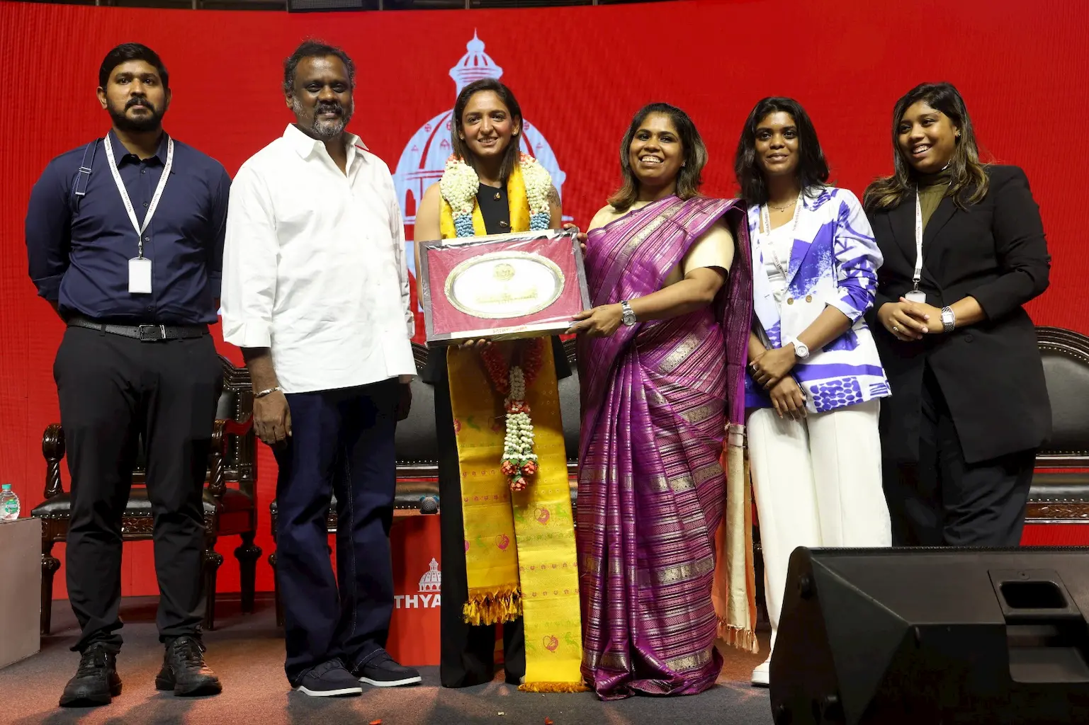 Indian women's cricket captain Harmanpreet Kaur being felicitated on stage at Sathyabama University in Chennai, receiving a framed memento while standing with university dignitaries